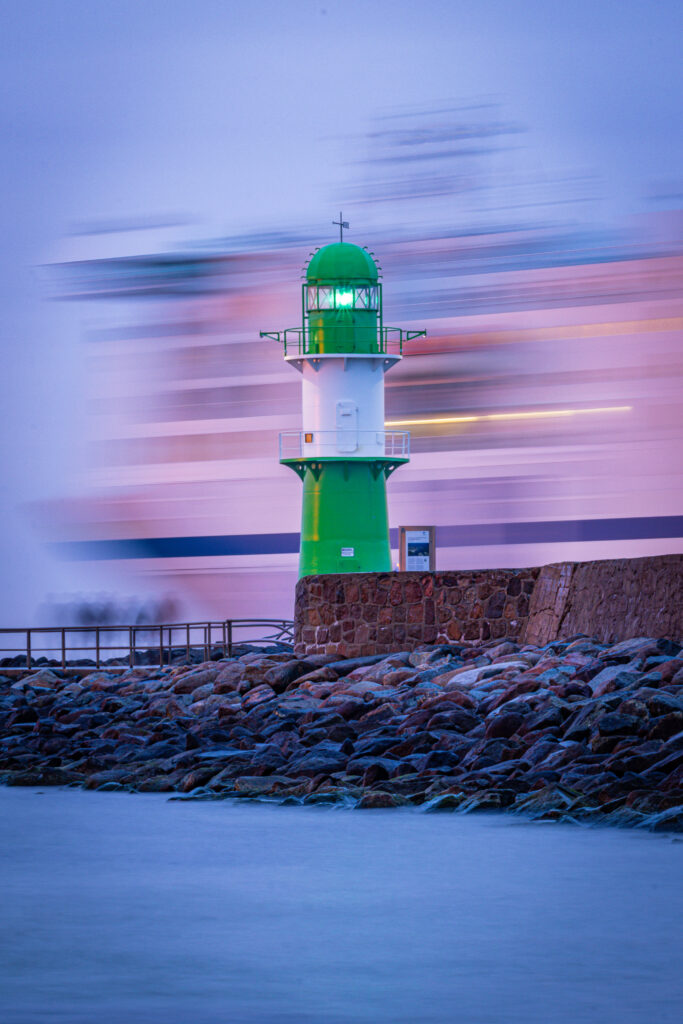 Grünes Signallicht am Alten Strom, Warnemünde, mit vorbeifahrendem Schiff im Hintergrund